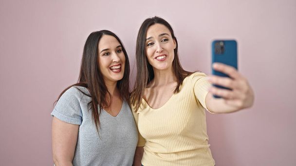 Két nő mosolygós magabiztos, hogy szelfi okostelefonnal izolált rózsaszín háttér - Fotó, kép