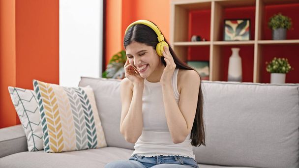 Joven mujer hispana hermosa escuchando música sentada en el sofá en casa - Foto, Imagen