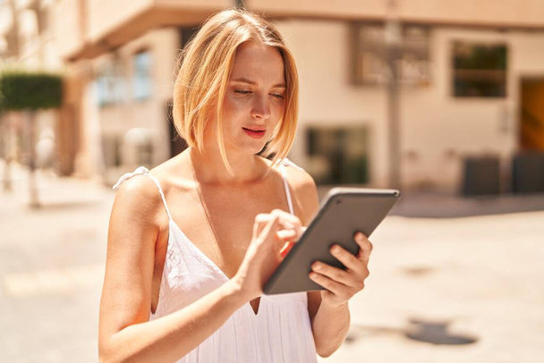 Jeune femme blonde utilisant touchpad avec une expression sérieuse à la rue - Photo, image