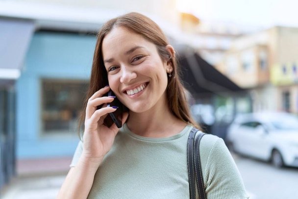 Fiatal gyönyörű nő mosolyog magabiztos beszél az okostelefonon az utcán - Fotó, kép