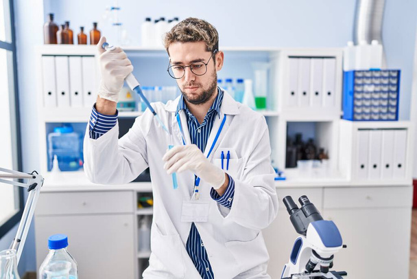 Mladý muž vědec nalévání kapaliny na zkumavky v laboratoři - Fotografie, Obrázek