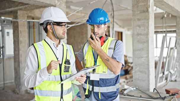Deux hommes constructeurs parler sur talkie walkie document de lecture sur le chantier de construction - Photo, image