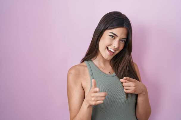 Hispanic woman standing over pink background pointing fingers to camera with happy and funny face. good energy and vibes.  - Foto, immagini