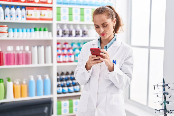 Joven bella mujer hispana farmacéutica usando smartphone trabajando en farmacia - Foto, imagen
