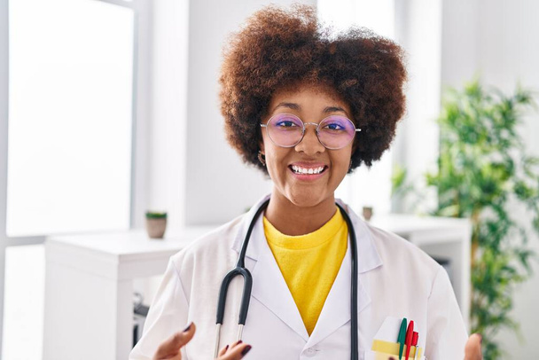 Африканская американка в форме врача улыбается уверенно стоя в клинике - Фото, изображение