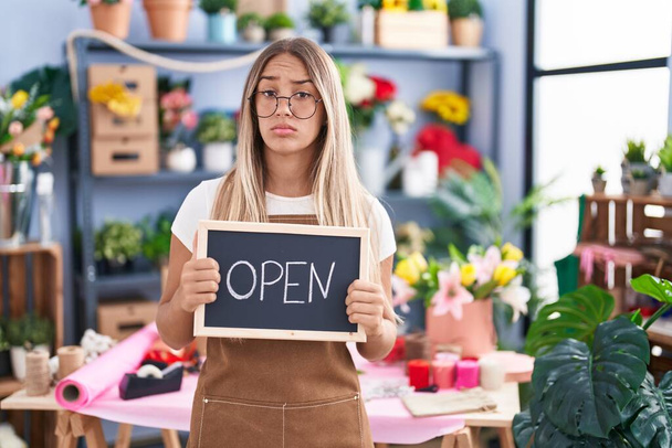 Young blonde woman working at florist holding open sign skeptic and nervous, frowning upset because of problem. negative person.  - Foto, Imagen