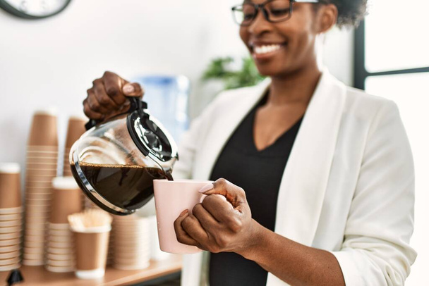 Afroamerykanka kobieta biznes pracownik nalewanie kawy na filiżankę w biurze - Zdjęcie, obraz