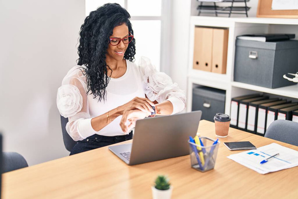 Afroamerykanka kobieta biznes pracownik za pomocą laptopa patrząc zegarek w biurze - Zdjęcie, obraz