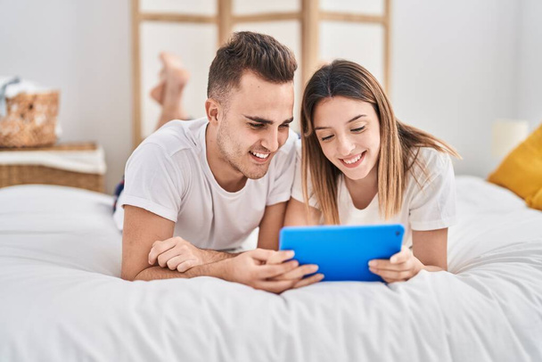 Man and woman couple watching video on touchpad lying on bed at bedroom - Photo, image