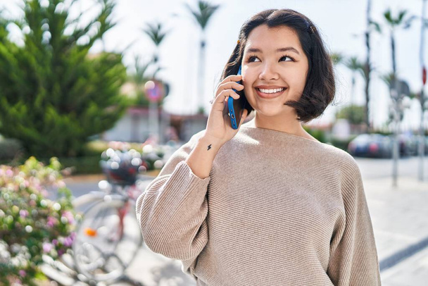 Gülümseyen genç bir kadın caddedeki akıllı telefondan konuşuyor. - Fotoğraf, Görsel