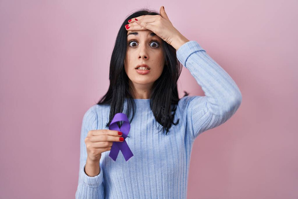 Mujer hispana sosteniendo la conciencia de la cinta púrpura estresada y frustrada con la mano en la cabeza, cara sorprendida y enojada  - Foto, Imagen