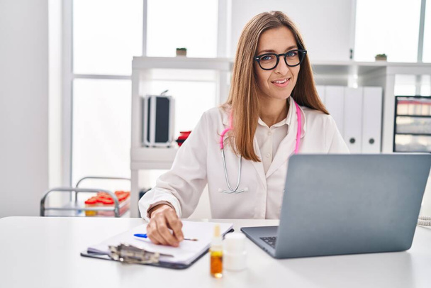 Young woman wearing doctor uniform writing on clipboard working at clinic - Φωτογραφία, εικόνα