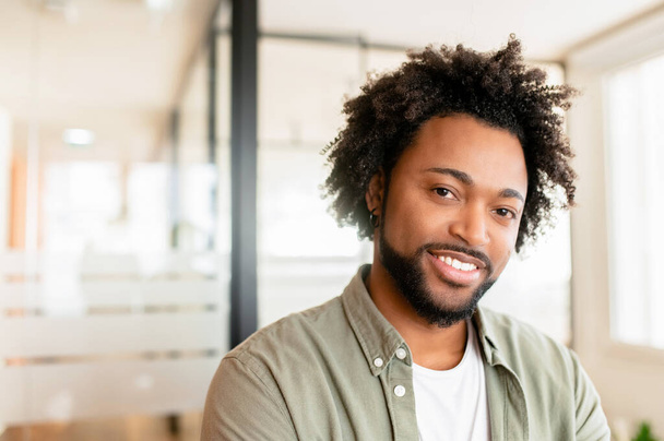 Közelkép portré magabiztos mosolygós üzletemberről, aki a modern coworking irodában áll, pózol és a kamerába néz, göndör afro-amerikai férfi vállalkozó, irodai alkalmazott - Fotó, kép