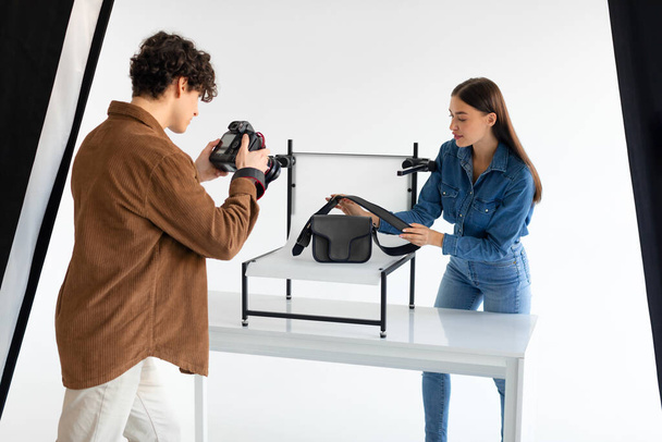 The art of teamwork. Professional photographer and his assistant doing content photoshoot for female bags, woman helping while working in team in photostudio - Photo, Image