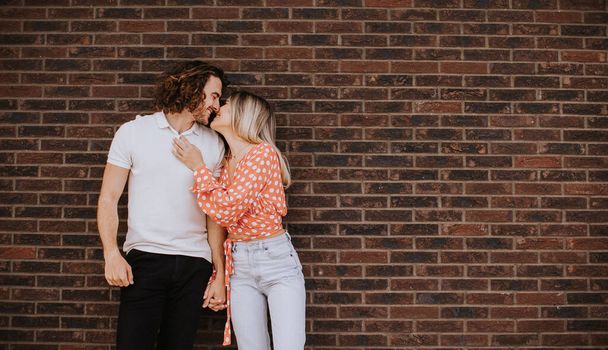 Handsome ymiling young couple in love in front of house brick wall - Fotoğraf, Görsel
