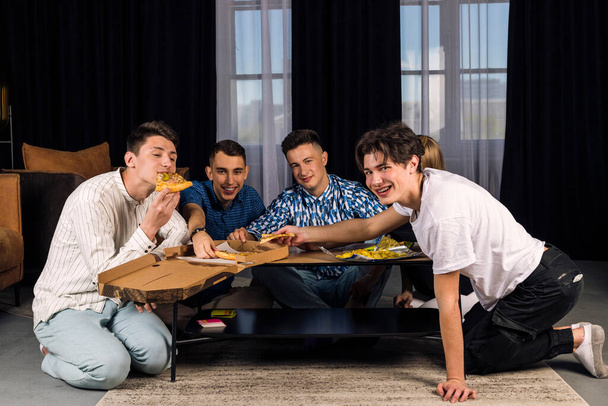 Five friends spending time together, having fun, playing table games and eating fast food and snacks. Small group of friend in a living room. - Foto, immagini