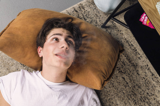 Junger Mann liegt auf dem Boden auf einem Kissen und raucht Dampf. - Foto, Bild