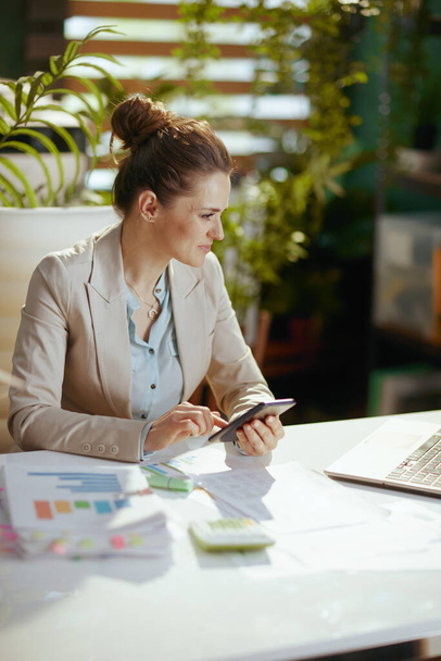 modern bookkeeper woman in a light business suit in modern green office using smartphone. - Фото, зображення