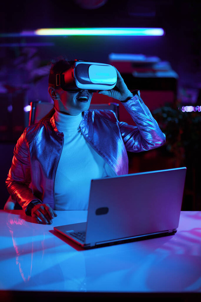 Neon metaverse futuristic concept. smiling stylish female in virtual reality goggles in modern office. - Foto, Imagen
