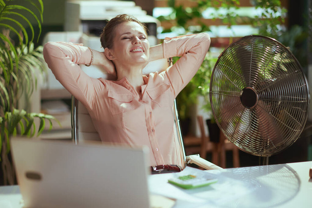 Sustainable workplace. smiling modern small business owner woman in modern green office with electric fan and laptop. - Foto, Imagem