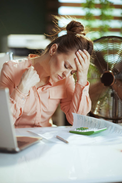 Sustainable workplace. unhappy modern 40 years old woman employee at work with electric fan. - Фото, зображення