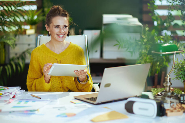 smiling modern small business owner woman in yellow sweater with tablet PC and laptop in the modern green office. - Foto, Bild