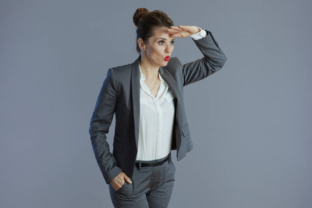 surprised modern 40 years old business woman in gray suit looking into the distance isolated on grey. - Foto, Imagen