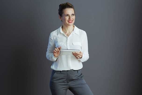 smiling middle aged small business owner woman in white blouse using applications on tablet PC isolated on gray background. - Foto, immagini