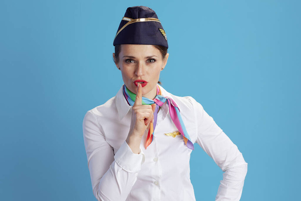 stylish air hostess woman against blue background in uniform showing shh gesture. - Foto, Imagen