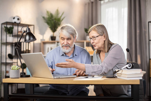 Elegant senior lady in glasses and gray-haired elderly man utilizing portable computer for distant work at home. Efficient freelancers studying details of temporary contract on digital screen. - Foto, immagini