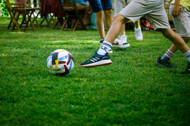 Berlin, Germany. May 1, 2022 Boys, children, teenagers play soccer on the green grass on a football field. Active sports in the fresh air. Kids legs in the motion. PLaying with a white ball Summer fun - Foto, Bild