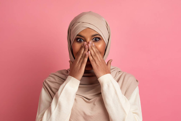 Omg. Mujer musulmana sorprendida en Hijab cubriendo la boca con las manos en asombro, mujer islámica emocionada feliz reaccionando emocionalmente a las buenas noticias, posando sobre fondo de estudio rosa, espacio de copia - Foto, Imagen