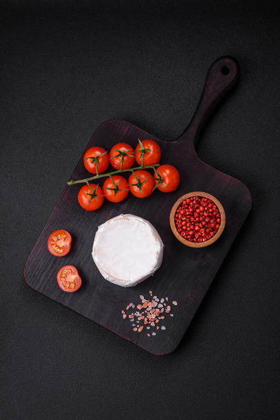 Delicioso queijo brie fresco na forma de uma mini cabeça com tomates cereja em um fundo de concreto escuro - Foto, Imagem