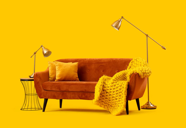Gemütliches braunes Sofa mit Kissen und Karo auf gelbem Hintergrund - Foto, Bild