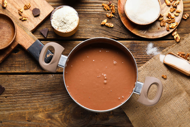 Pot with dough and ingredients for preparing chocolate brownie on wooden background - Фото, зображення