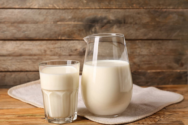 Jug and glass of fresh milk on wooden background - Фото, изображение