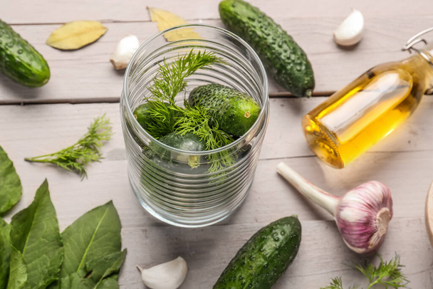 Jar with fresh cucumbers and ingredients for preservation on light wooden background - Photo, Image