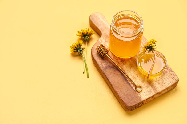 Board, jar and bowl with dandelion honey on yellow background - Photo, Image