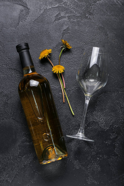 Bottle and glass of dandelion wine on black background - Foto, afbeelding