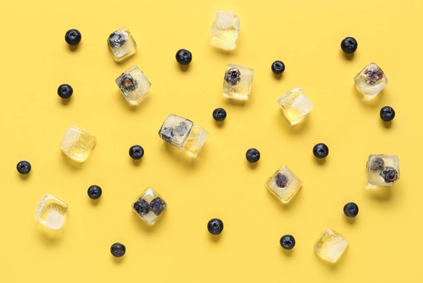 Ripe blueberry frozen in ice cubes and fresh berries on yellow background - Fotó, kép