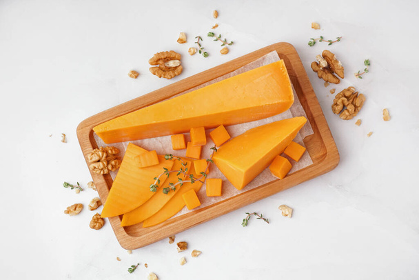 Wooden board with tasty cheddar cheese on light background - Foto, Imagen