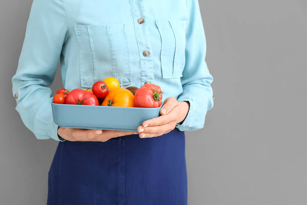 Woman holding bowl with different fresh tomatoes on grey background, closeup - Foto, Imagem