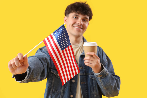 Junger Mann mit USA-Flagge und Tasse Kaffee auf gelbem Hintergrund - Foto, Bild