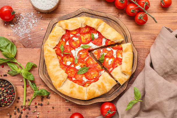 Board with tasty tomato galette and basil on wooden background - Photo, Image
