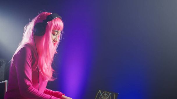 Dj in pink hair mixing electronic sound using mixer console, dancing and having fun in club with fans during performance. Asian artist performing techno music using professional audio equipment - Foto, afbeelding