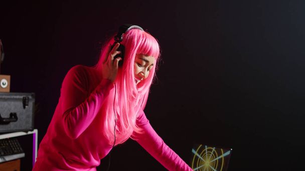 Cheerful artist working as dj playing song at turntables, mixing techno music with eletronic using audio equipment. Musician with pink hair having fun in performing in club at night time - Foto, Bild