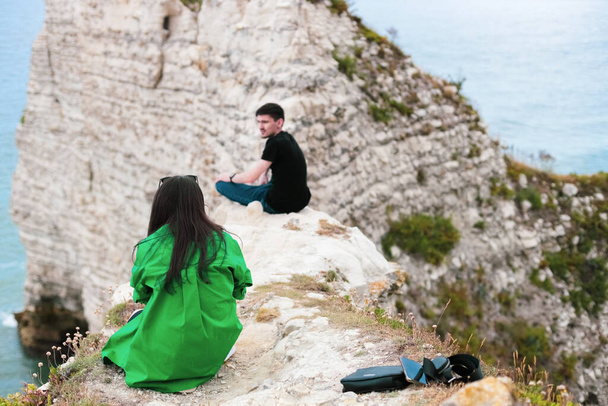 One young caucasian couple of tourists from the back sits high in the mountains and takes pictures on a smartphone near the north sea in Etretat, Normandy, France, close-up view from below. - Φωτογραφία, εικόνα