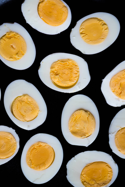 Boiled eggs pattern on a black background viewed from above. Top view. Egg half. Yolk. Fresh farm chicken boiled half cut eggs pattern. Healthy food creative minimal concept. High quality photo. - 写真・画像