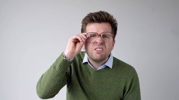 Młody Europejczyk ze słabym wzrokiem patrzy przez okulary, próbując dostrzec informacje, które go interesują. Zdjęcia studyjne - Zdjęcie, obraz