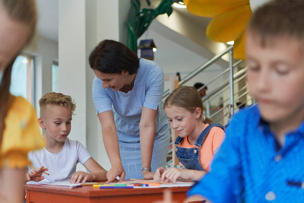 Creative kids during an art class in a daycare center or elementary school classroom drawing with female teacher - Φωτογραφία, εικόνα